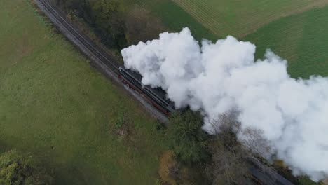 Aerial-over-head-view-of-an-antique-restored-steam-locomotive-traveling-thru-autumn-trees-as-it-is-blowing-white-smoke-and-steam