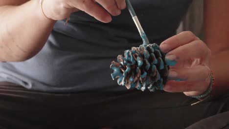 Close-up-on-caucasian-woman's-hands,-painting-and-decorating-a-pine-cone-with-blue-light-colour,-udsing-a-brush-120fps