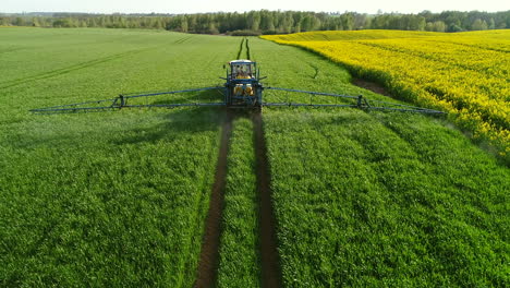 Tractor-with-trailer-and-wide-metal-arm-with-nozzles-spraying-pesticides-over-the-green-field