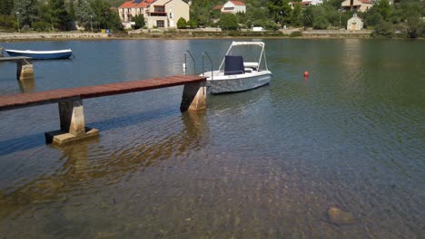 View-of-a-single-boat-floating-in-shallow-waters-at-the-end-of-a-very-narrow-wooden-pier-in-Vela-Luka,-Croatia