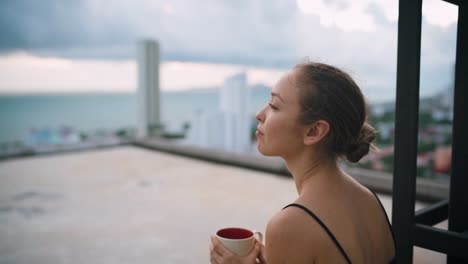 Close-up-portrait-shot-of-young-woman-sitting-on-roof-and-drinking-coffee-while-looking-to-the-side