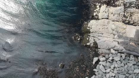 Topdown-reveal-shot-of-blue-water-rocky-beach