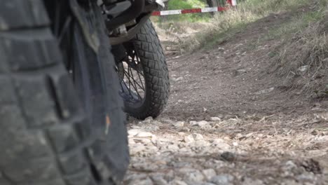 Close-up-on-motorcycle-wheels,-static-on-soil-ground,-pull-focus-from-wheels-to-road-barrier-in-the-background-120fps