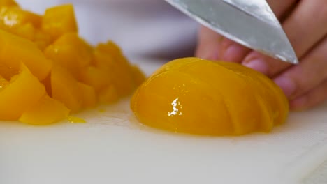 Close-up-of-cutting-pickled-peaches-on-white-cutting-board-with-stainless-steel-knife