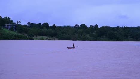 Fisherman-trying-to-fish-on-a-flooded-lake-with-his-motorized-longboat-in-Wangnamkaew,-Nakhon-Ratchasima,-Thailand