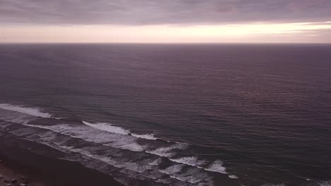 Beautiful-purple-sunset-over-the-waves-of-Ecuador-by-Olon-Beach--aerial-ascend