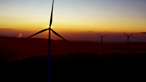 Silhouettes-of-Wind-Turbines-Spinning-in-Front-of-Scenic-Sunset-Sunlight,-Aerial-View