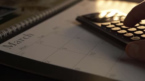 Hand-using-calculator-on-March-calendar-close-up