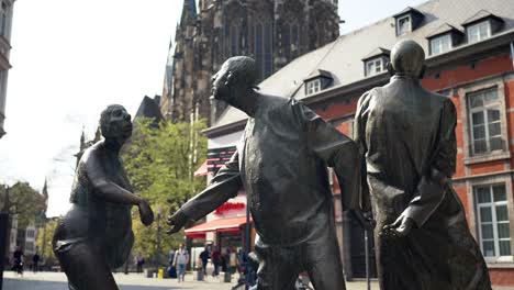 Bronze-statue-with-people-and-whirl-pool-in-Aachen,-Germany,-called-Circulation-of-Money-with-the-Aachener-Dom-Cathedral-in-background