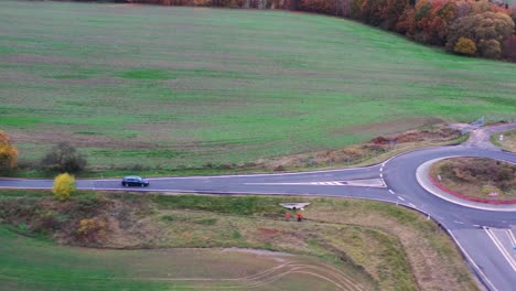 Aerial-View-of-Lonely-Car-on-Countryside-Road-in-Autumn-Approaching-Roundabout