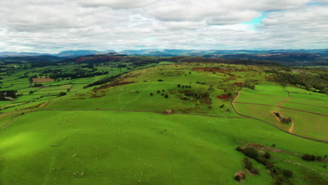 Aerial-dolly-shot-looking-over-the-green-hills-and-farmland-in-the-English-Lake-District,-bright-daylight-with-white-clouds