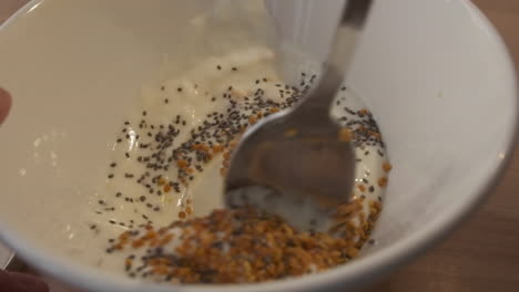 Mixing-Cereals-With-Yogurt-And-Chia-Seeds-In-A-Bowl-Using-A-Spoon---close-up,-slow-motion