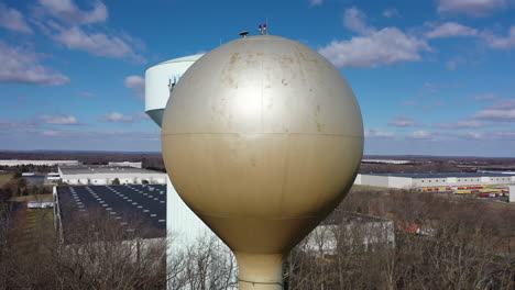 An-aerial-shot-orbiting-a-silver-water-tower-with-another-blue-one-in-the-background