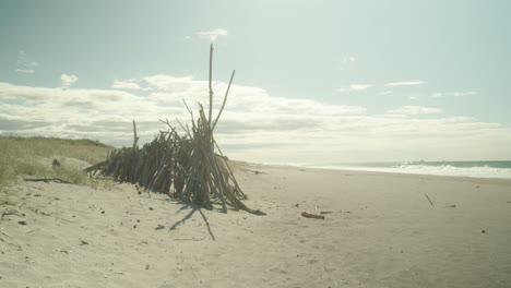 Teepee,-structure-made-of-wooden-sticks,-on-beach-in-golden-sunshine