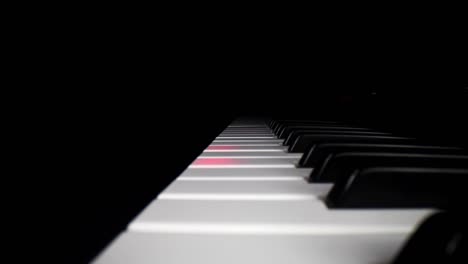 Low-profile-wide-angle-macro-of-electronic-keyboard---static-shot-of-keyboard-as-the-song-assist-lights-the-keys-a-red-glow,-then-moving-backwards-slightly-as-song-continues-to-play