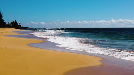HD-Hawaii-Kauai-slow-motion-static-wide-shot-of-beach-on-left-and-ocean-waves-washing-in-from-right-to-left-and-across-lower-frame-on-a-sunny-day