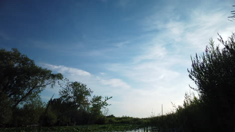 A-motion-time-lapse-of-the-sky,-fast-moving-clouds,-and-reveal-of-a-summer-pond-during-the-daytime