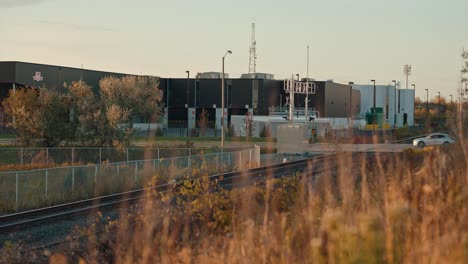 Autos-Fahren-über-Bahnübergangsgleise-Am-Bahnhof-In-Einer-Industriellen-Stadt-Mit-Goldenem-Morgensonnenaufgang-Und-Funktürmen-In-Der-Ferne,-Filmisches-Toronto,-Ontario,-Markham-TTC,-Filmisches-Prores-4k