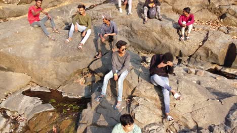 Aerial-view-of-a-group-of-young-Indian-boys-sitting-on-big-rocks-near-a-small-dried-waterfall-in-forest,-Drone-shot-of-friends-sitting-on-dried-waterfall-and-big-rocks-in-forest-video-background