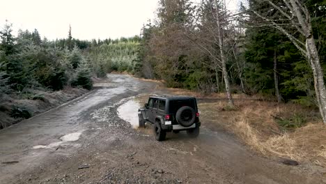 A-lone-black-Jeep-dives-into-a-deep-mud-puddle,-slow-motion-aerial,-illustrative-editorial