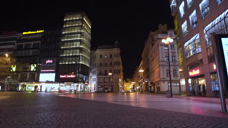 The-bottom-of-the-Wenceslas-square-in-Prague,-Czechia-at-night,-shopping-centres-lit-by-neon-lights,-the-whole-area-empty-with-no-people-due-to-a-Covid-19-lockdown,-streets-lit-by-lights,-pan-shot
