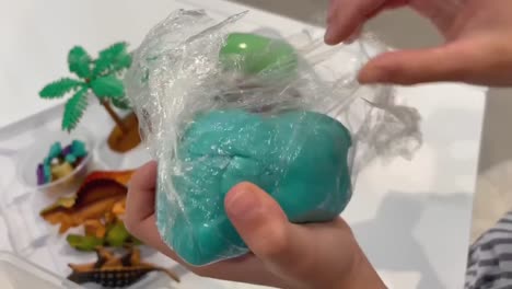 Child-opening-up-home-made-playdough-out-of-a-dinosaur-themed-sensory-bin