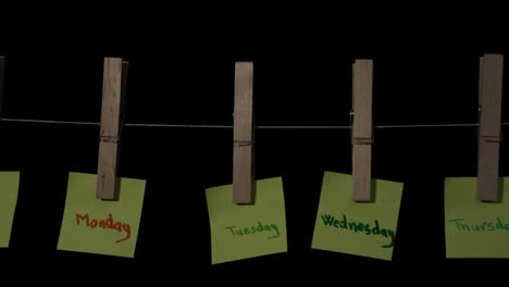 Days-of-the-week-in-yellow-sticker-labels-hanging-on-wooden-sticks-with-black-background