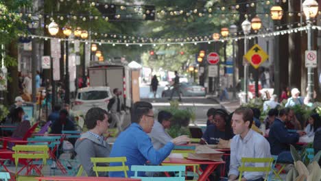 A-panning-shot-of-a-diverse-crowd-of-young-professionals-eat-lunch,-relax-in-the-shade,-and-chat-while-walking-around-historic-downtown-Atlanta-during-lunch-on-a-busy-summer-work-day