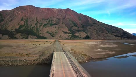 Spectacular-backward-flight-above-empty,-desolate,-remote-and-rural-Yukon-wilderness-Alaska-highway-by-majestic,-colorful,-imposing-and-impressive-Sheep-mountain-range-by-Kluane-lake,-aerial-pull-back