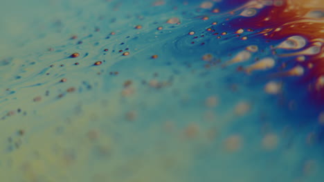 Macro-shot-of-small-particles-flowing-into-a-rainbow-colored-liquid