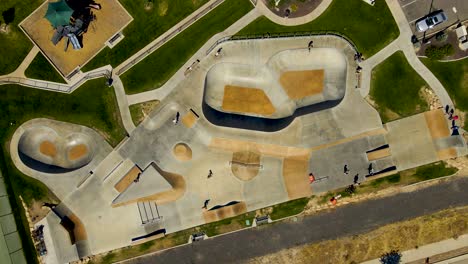 Ascending-rotating-aerial-view-of-a-community-skate-park-with-kids-on-skateboards-and-scooters-in-summer