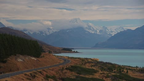 Cars-driving-along-the-coast-of-glacial-Lake-Pukaki,-towards-the-Southern-Alps-and-Mount-Cook-in-New-Zealand-South-Island