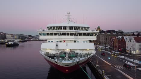 Aerial-ascending-shot-over-Hurtigruten-cruise-ship-bow-moored-at-Bergen-harbour-at-morning-dusk-lights