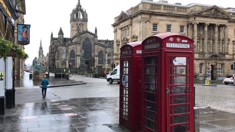 People-walk-past-red-phone-boxes-near-St-Giles-Cathedral-on-the-Royal-Mile-in-Edinburgh,-Scotland,-UK