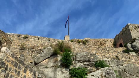 Blick-Von-Unten-Auf-Die-Kroatische-Flagge,-Die-Auf-Der-Antiken-Festung-Klis-Weht,-Dem-Berühmten-Drehort-Von-Game-Of-Thrones