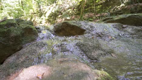 Sauberes-Süßwasser-Des-Baches,-Der-An-Sommertagen-über-Moosige-Felsen-Fließt
