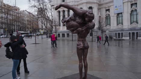 Vista-De-Una-Mujer-Gordita-Besando-A-Un-Hombre-Escultura-Frente-A-La-Oficina-De-Correos-En-Madrid,-España-Con-Turistas-Paseando-Y-Tomando-Fotos---Tiro-Completo