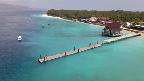 Epic-aerial-circling-shot-of-Gili-Meno-island-with-girl-walking-on-wooden-pier,forest-and-crystal-clear-blue-water