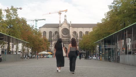 Two-young-women-talking-and-walking-forward-at-the-Place-de-Saint-Catherine-in-Brussels,-Belgium-on-warm-summer-day