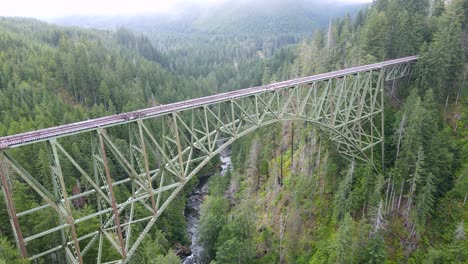 Passing-over-the-abandoned-rail-bridge-crossing-and-a-rugged-forest-canyon,-Vance-Creek,-Washington
