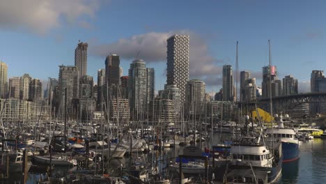 Panorama-of-marina-where-small-boats-are-anchored-in-the-water-in-front-of-cityscape-high-rise-buildings-in-the-background-blue-sky-clouds-bridge-metropolis