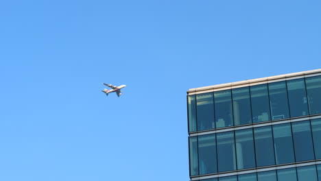 Big-Passenger-Airplane-Flying-over-Modern-Office-Building,-Low-Angle