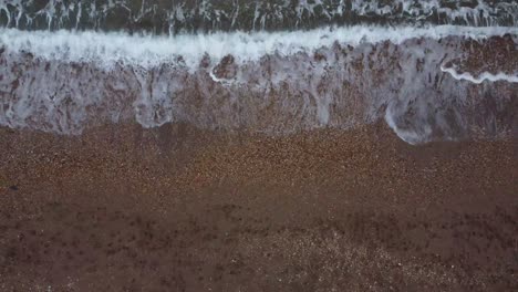 A-slow,-rising,-4k-drone-shot-of-waves-coming-onto-a-shingle-beach-in-South-Devon