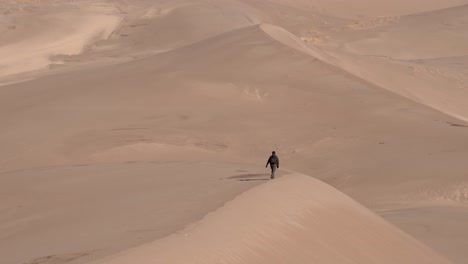 Man-walking-over-sand-dunes-on-a-sunny-day