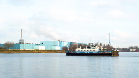 Amsterdamer-Fähre-überquert-Den-Fluss-Mit-Einem-Rauchenden-Industriegebäude-Im-Hintergrund
