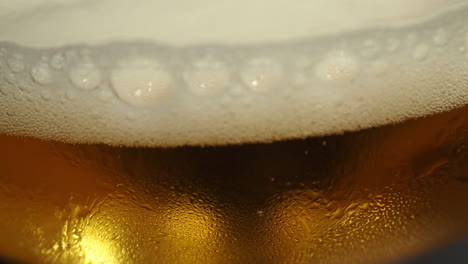 Cabeza-De-Cerveza-Espumosa-Bordeando-La-Bebida-Dorada-En-Una-Taza---Primer-Plano-Extremo