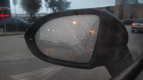 View-Of-A-Car-Passing-By-Through-Blurry-Wet-Left-Side-Mirror-Of-A-Parked-Car-On-A-Rainy-Day---POV,-static-shot
