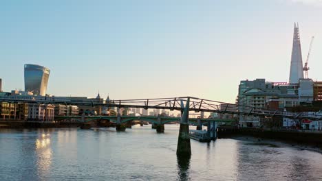 Aerial-slider-shot-of-man-running-on-Millennium-walking-bridge-over-thames-river-towards-city-of-London-at-sunrise-Low