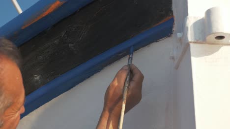 Painter-paints-trim-of-wooden-fishing-boat-slow-motion-blue-paint
