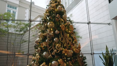 Elegante-Weihnachtsbaumpräsentation-In-Einem-Einkaufszentrum-Mit-Leuchtenden-Goldenen-Dekorationen-–-Nach-Unten-Geneigte-Aufnahme